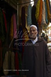 Image du Maroc Professionnelle de  Mohammed Ennaji âgé de soixante-dix ans, pose devant son atelier à Marrakech, il a commencé à pratiquer ce métier de teinturier à l’âge de dix ans, cela lui fait soixante ans de métier un des plus ancien voir le vétéran des teinturiers, son atelier est situé au centre du Souk des Teinturiers, appelé souk Sebbaghine, l'un des plus pittoresque de Marrakech situé dans la Médina, non loin de la source Mouassine, où quelques petits ateliers pratiquent encore de nos jours la teinture traditionnelle. Ce lieu très prisé des touristes et amateurs photos qui désire ardemment des images extrêmement colorées. Avec le temps il est devenu presque une des attractions touristique qui vaut le détour. Derrière Si Mohammed Ennaji des écheveaux de laines sèchent au soleil suspendu en l’air ou le long des murs, le 8 Décembre 2018. (Photo / Abdeljalil Bounhar)